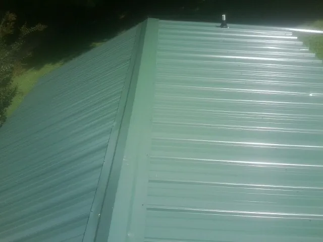 New green metal panels meeting at the ridge of a roof — Flat Roof Repair work by our crew in Hazlet