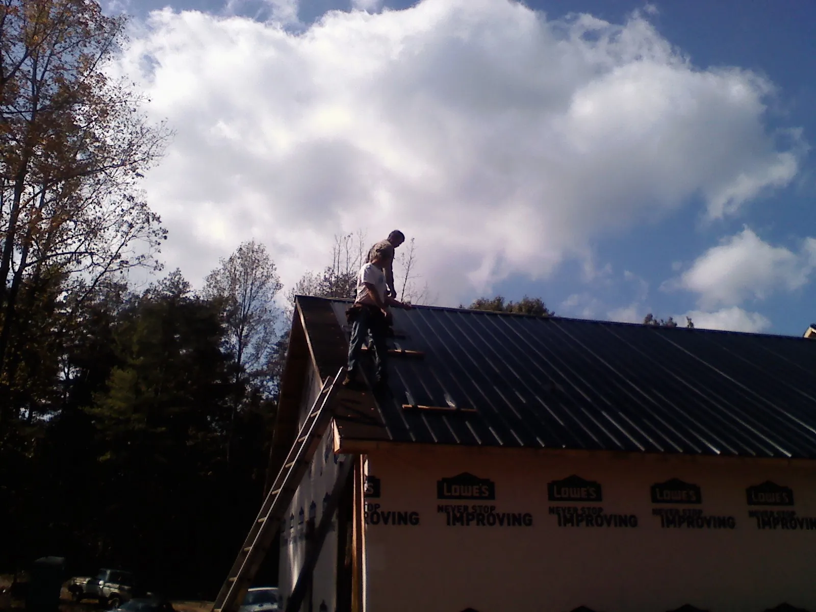 Roofer fastening dark metal panels high against a cloudy sky, from a Roof Inspection job in Hazlet
