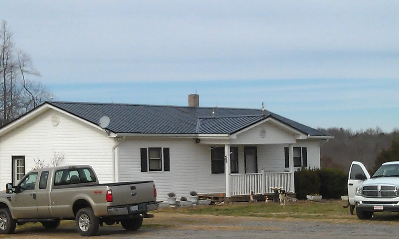 Finished dark metal roof on a white ranch home with work trucks parked in Hazlet